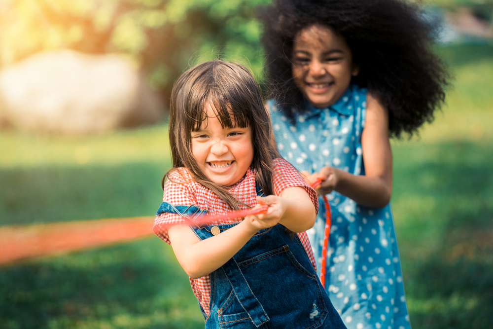 Happy children playing tug of war in the park.