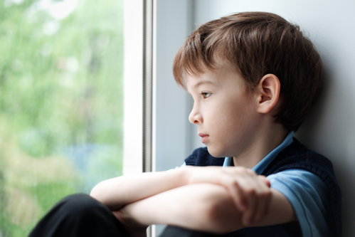 Sad boy sitting on window