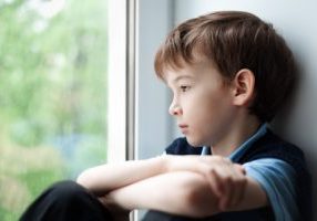 Sad boy sitting on window